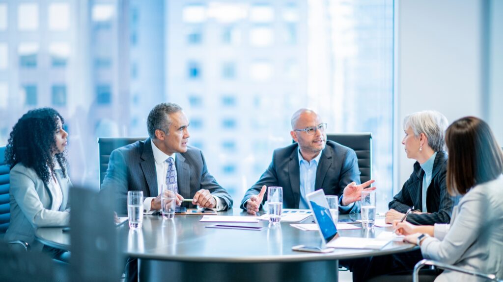 A group of bussiness people sit around a round desk and discuss.