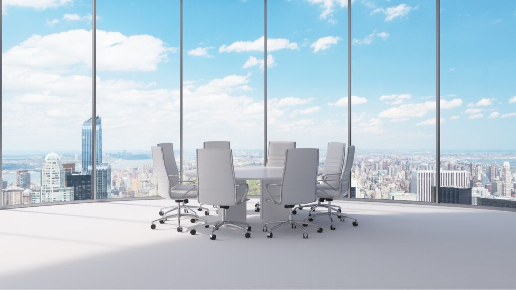 A desk surrounded by empty office chairs in a room with a view overlooking a city.
