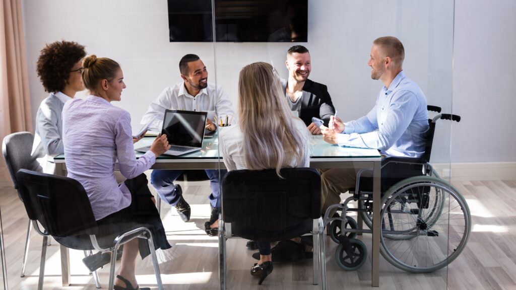 A group of business people sit around a table in a meeting, actively listening a guy in a wheelchair