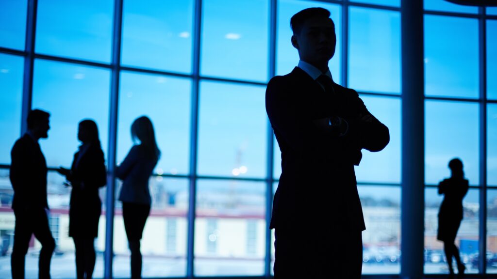 Silhouetted businessperson standing confidently with a team in the background.