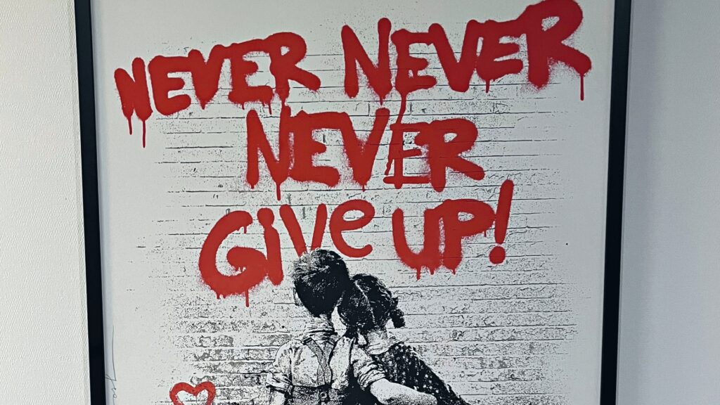An artwork where a boy and a girl look at a wall with graffiti on it that says 'Never never never give up'