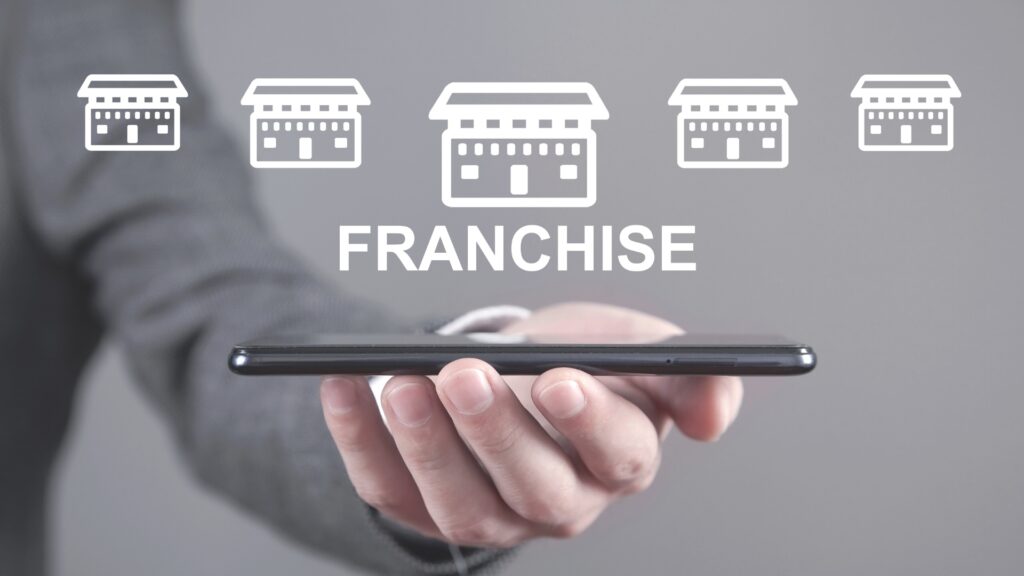 A hand holding a mobile phone with graphics of stores symbolising franchises