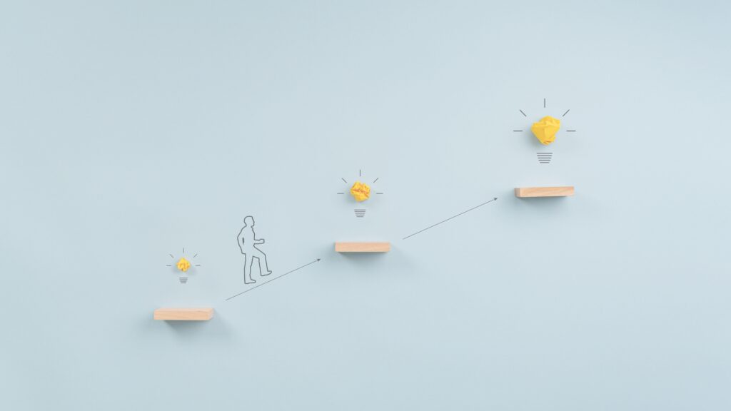 A person illustrated on a light blue background stepping up a series of increasing platforms with light bulbs above each step