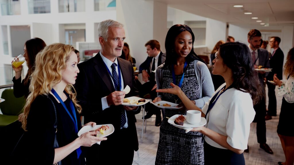 Four people in a semi circle, holding small plates of food, listening to one of them talk