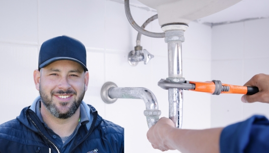 Smiling plumber standing next to a sink being repaired, showcasing professional plumbing services with a friendly demeanor