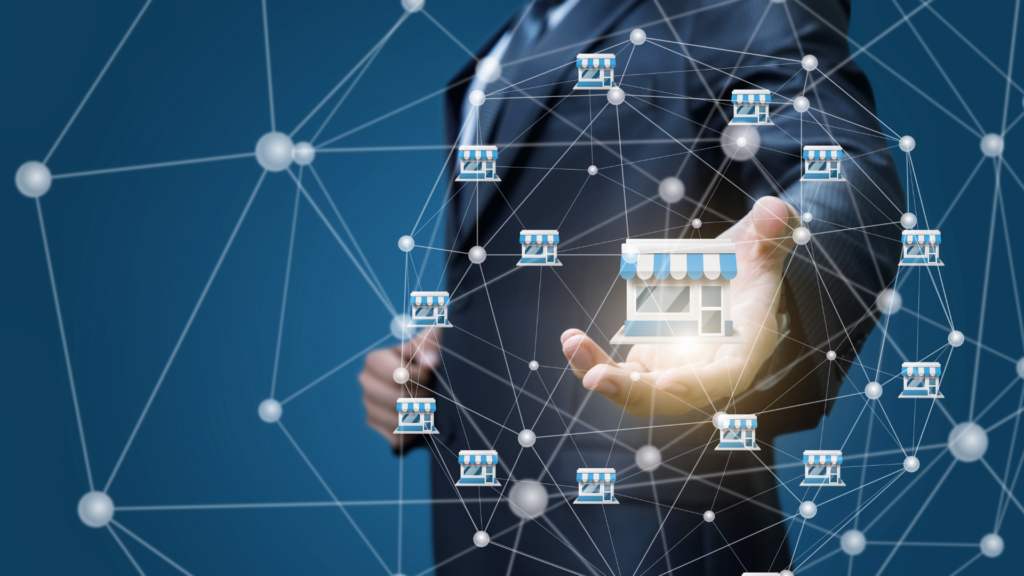 A businessperson's hand supporting a small storefront model, symbolizing franchising and expansion within a network, depicted on a blue background with interconnected nodes.