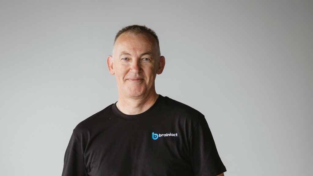 a man smiles at the camera with his business's shirt on
