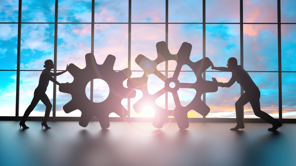 Silhouettes of two businesspeople pushing large gears, symbolizing teamwork and collaboration in business