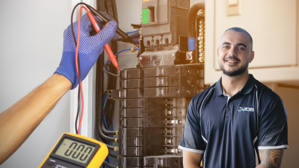 Electrician performing measurements with a multimeter, featuring a smiling technician from JDS
