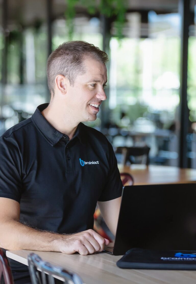 man smiles sitting in front of his laptop at a desk
