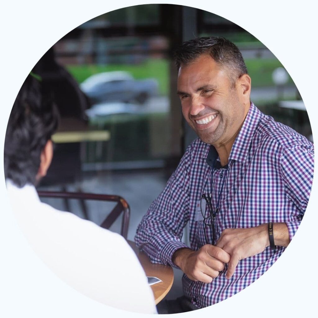 A man in a checkered shirt sits and laughs with another man