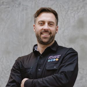 man stands in his uniform with arms crossed, smiling